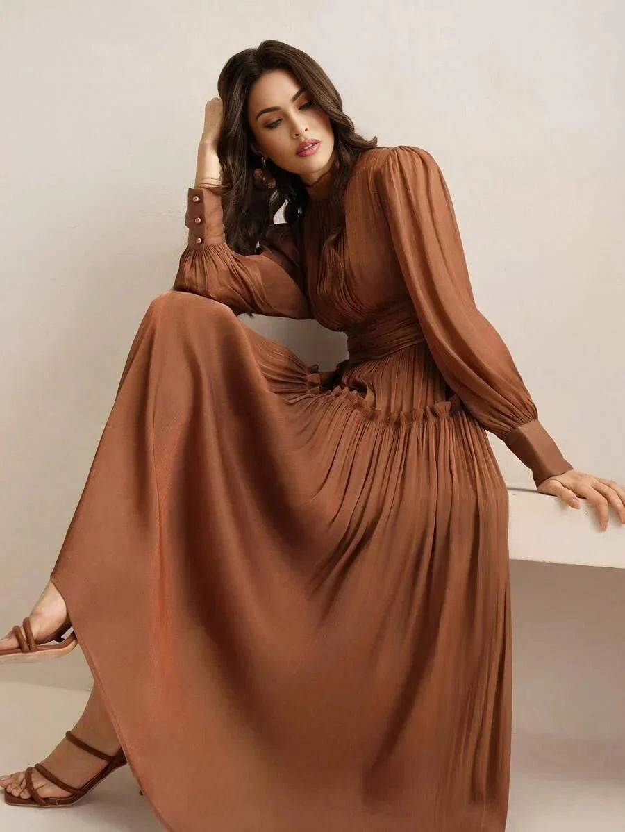 This graceful long-sleeved dress features a rich, earthy brown hue, accentuated by pleated detailing that enhances its flowy.