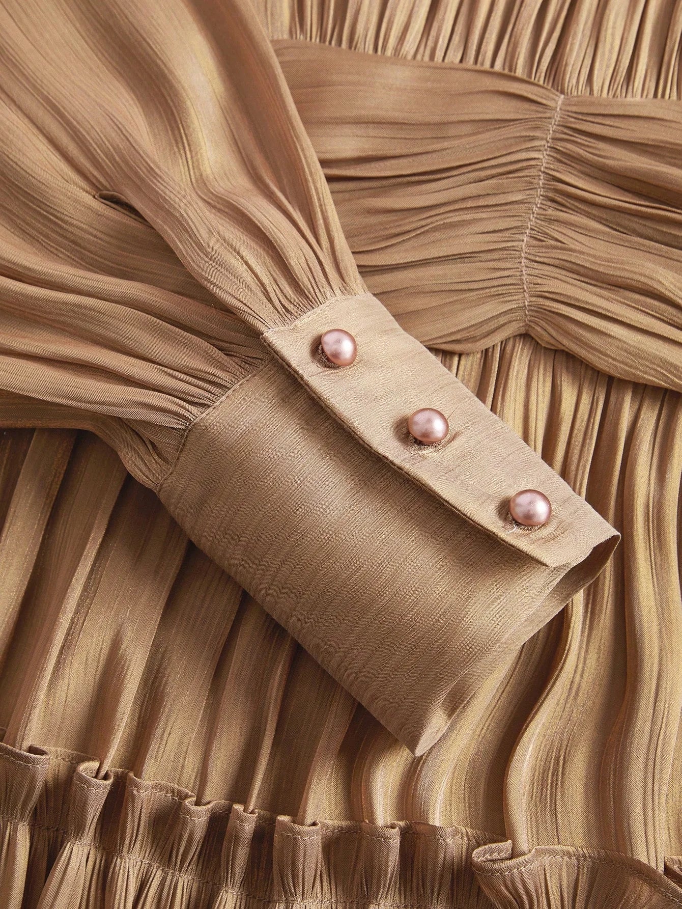 This elegant dress features a warm, golden-brown hue with soft pleats that create a flowing silhouette, accentuated by.