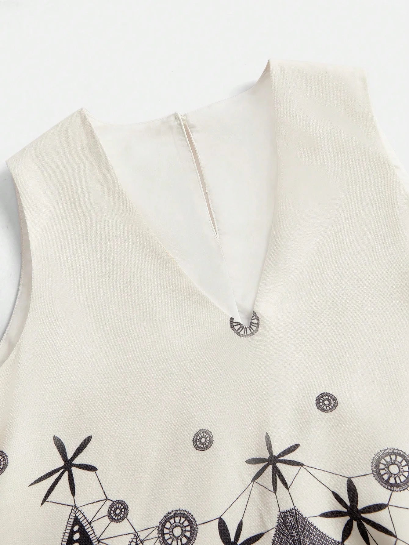 This elegant cream dress features a sophisticated V-neckline and delicate black embroidery, showcasing an intricate design.