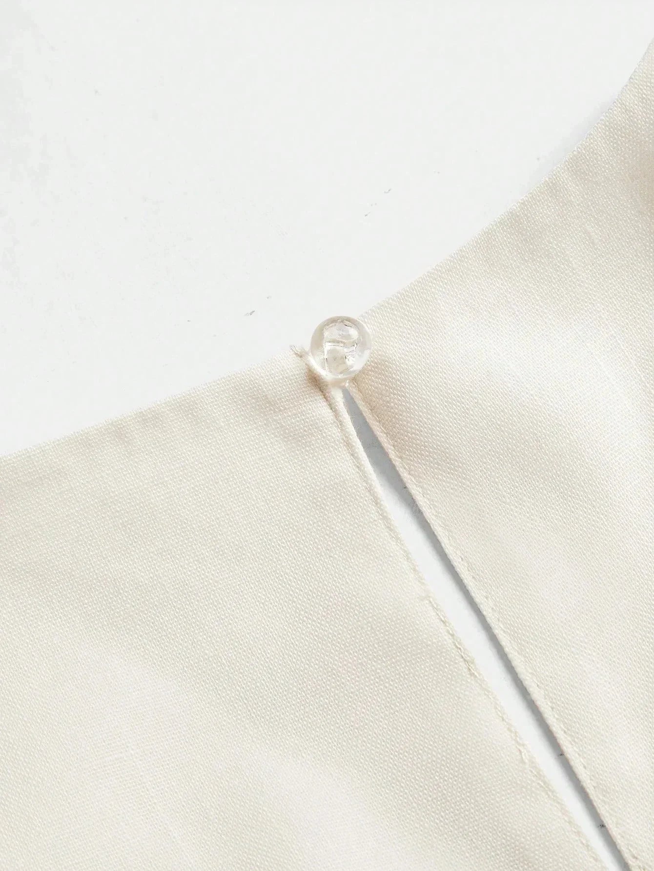 This elegant cream dress features a sleek, minimalist design with a delicate button detail at the neckline, crafted from a.