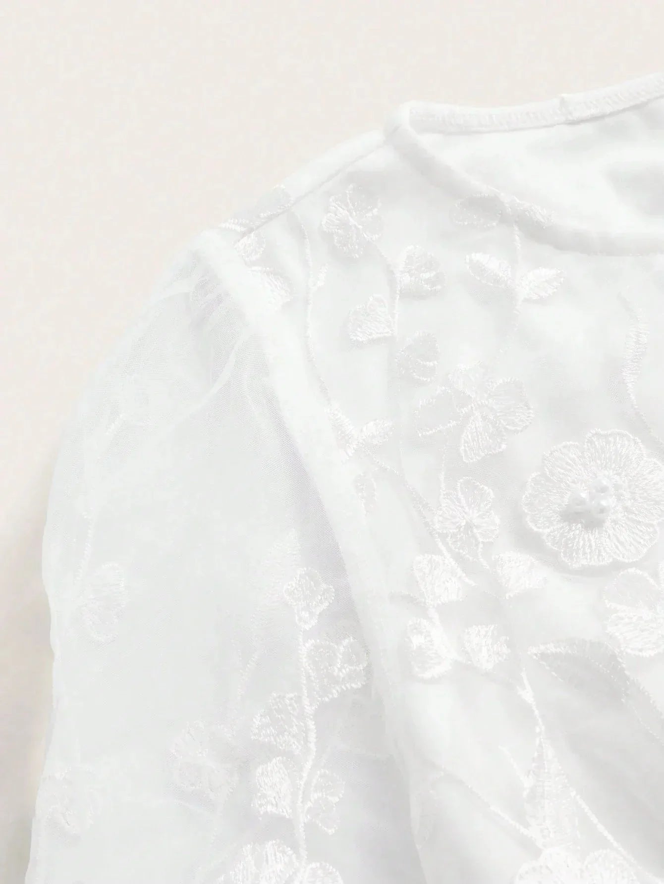 This elegant white dress features delicate floral embroidery on sheer fabric, creating a soft and romantic look. The.