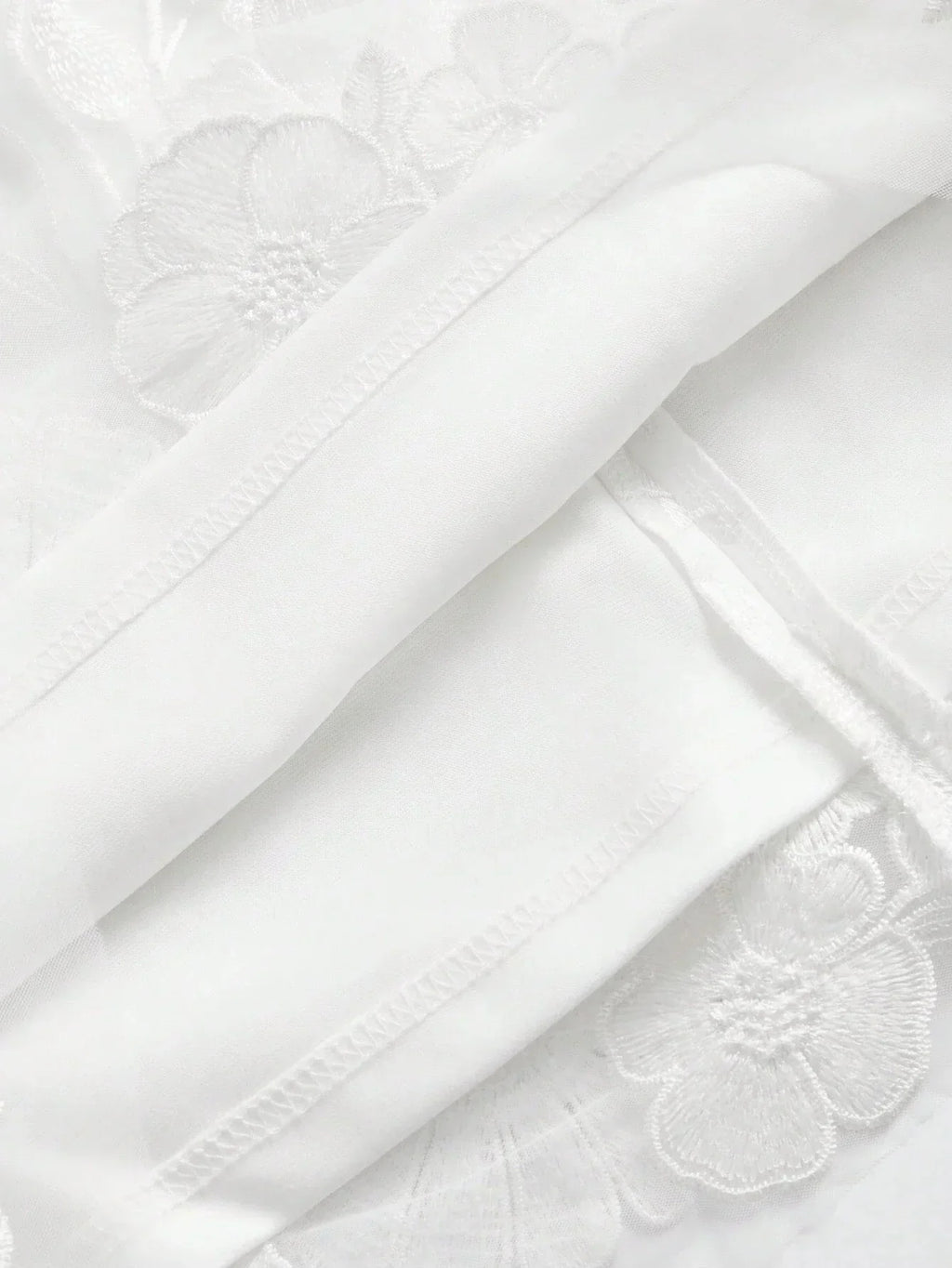A delicate white dress featuring intricate floral embroidery, crafted from lightweight fabric that offers a soft and airy.
