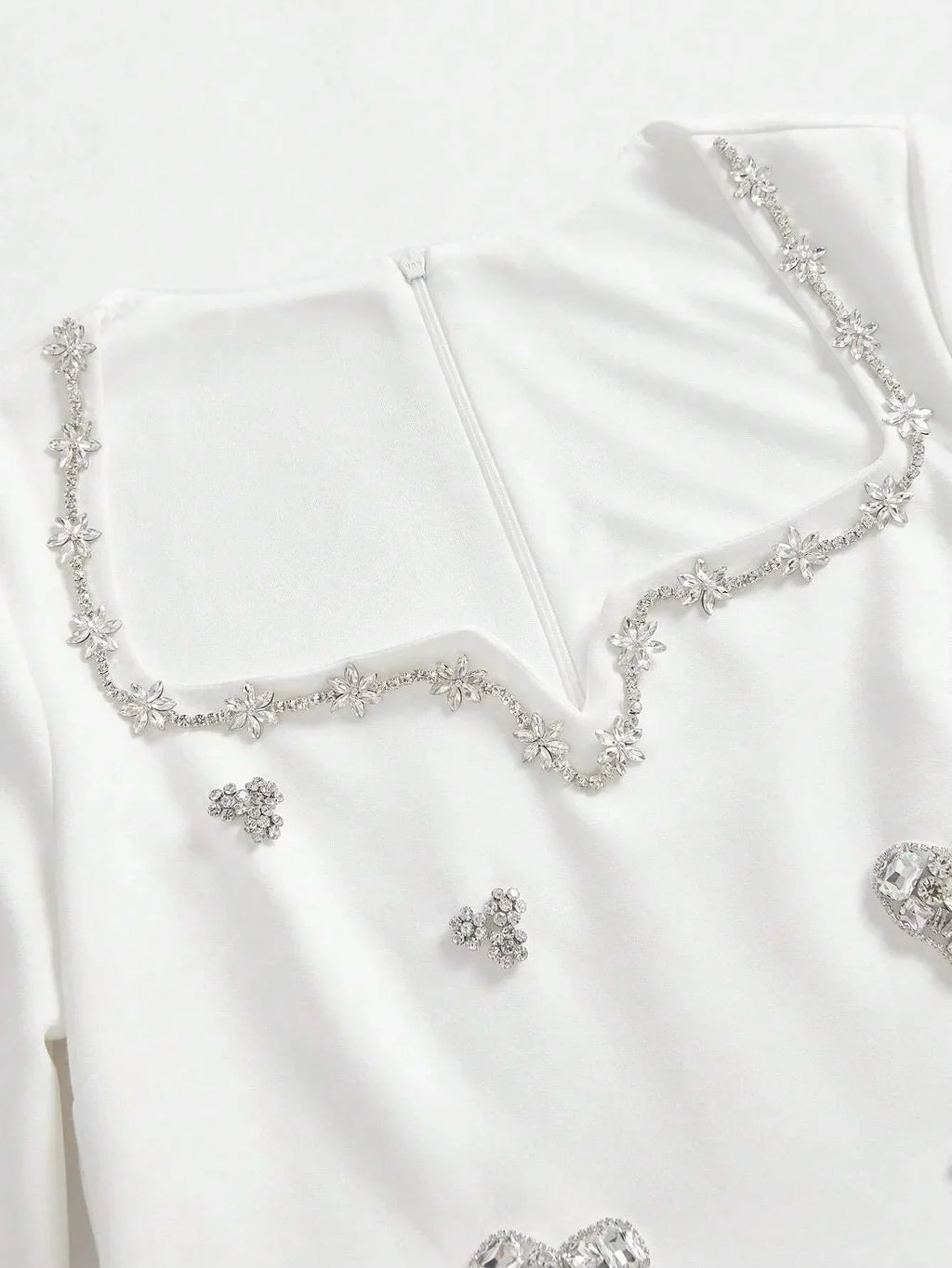 This elegant white dress features a sophisticated square neckline adorned with delicate floral embellishments and shimmering.
