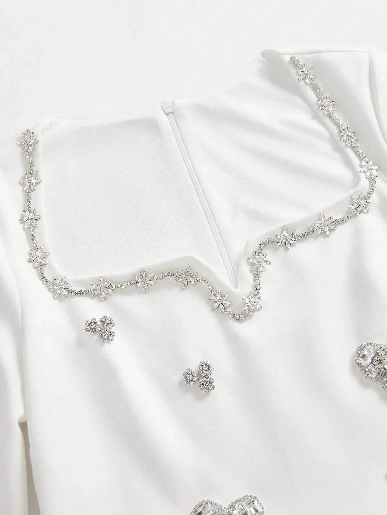 This elegant white dress features a sophisticated square neckline adorned with delicate floral embellishments and shimmering.