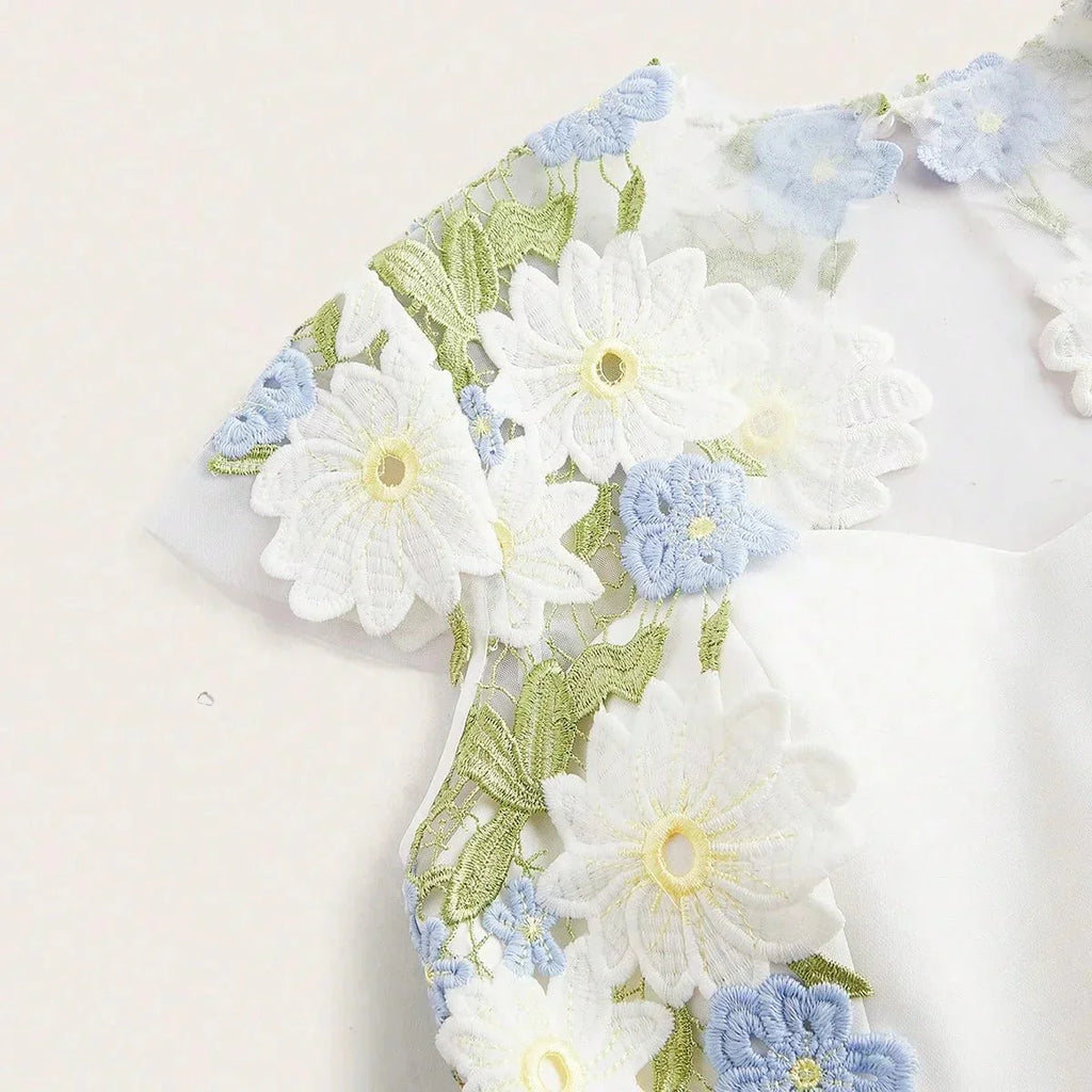 This elegant white dress features a delicate floral embroidery in soft blue and vibrant green, creating a fresh and romantic.