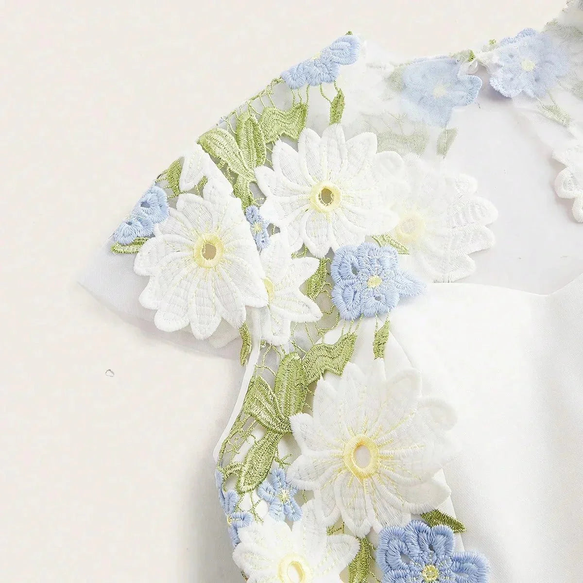This elegant white dress features a delicate floral embroidery in soft blue and vibrant green, creating a fresh and romantic.