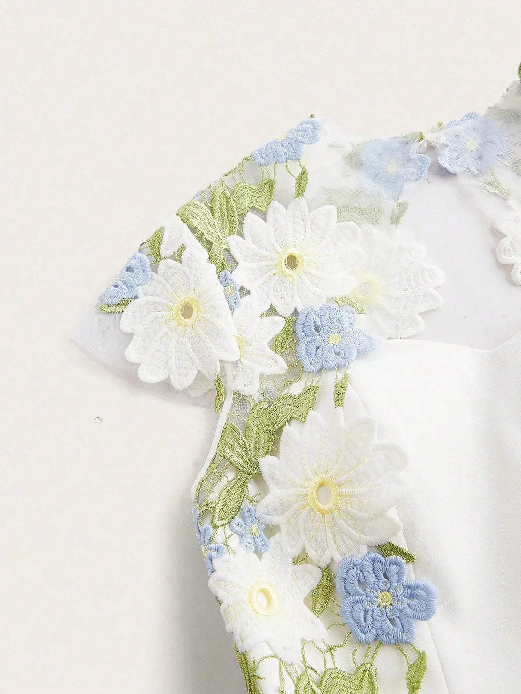 This enchanting white dress features delicate floral embroidery in soft blue and green hues, lending a fresh and romantic.