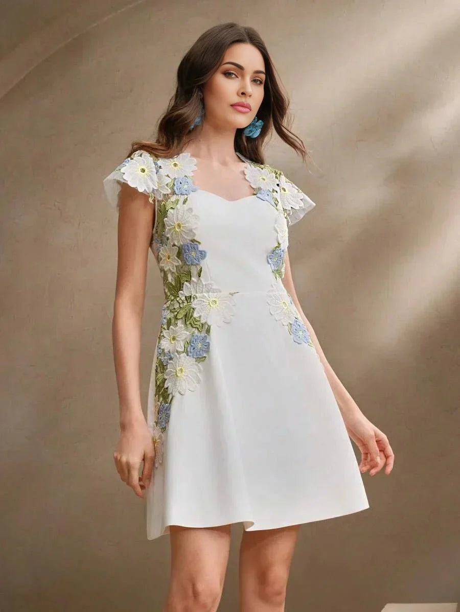 This charming white dress features delicate floral embroidery in soft blues and vibrant greens, creating a stunning contrast.