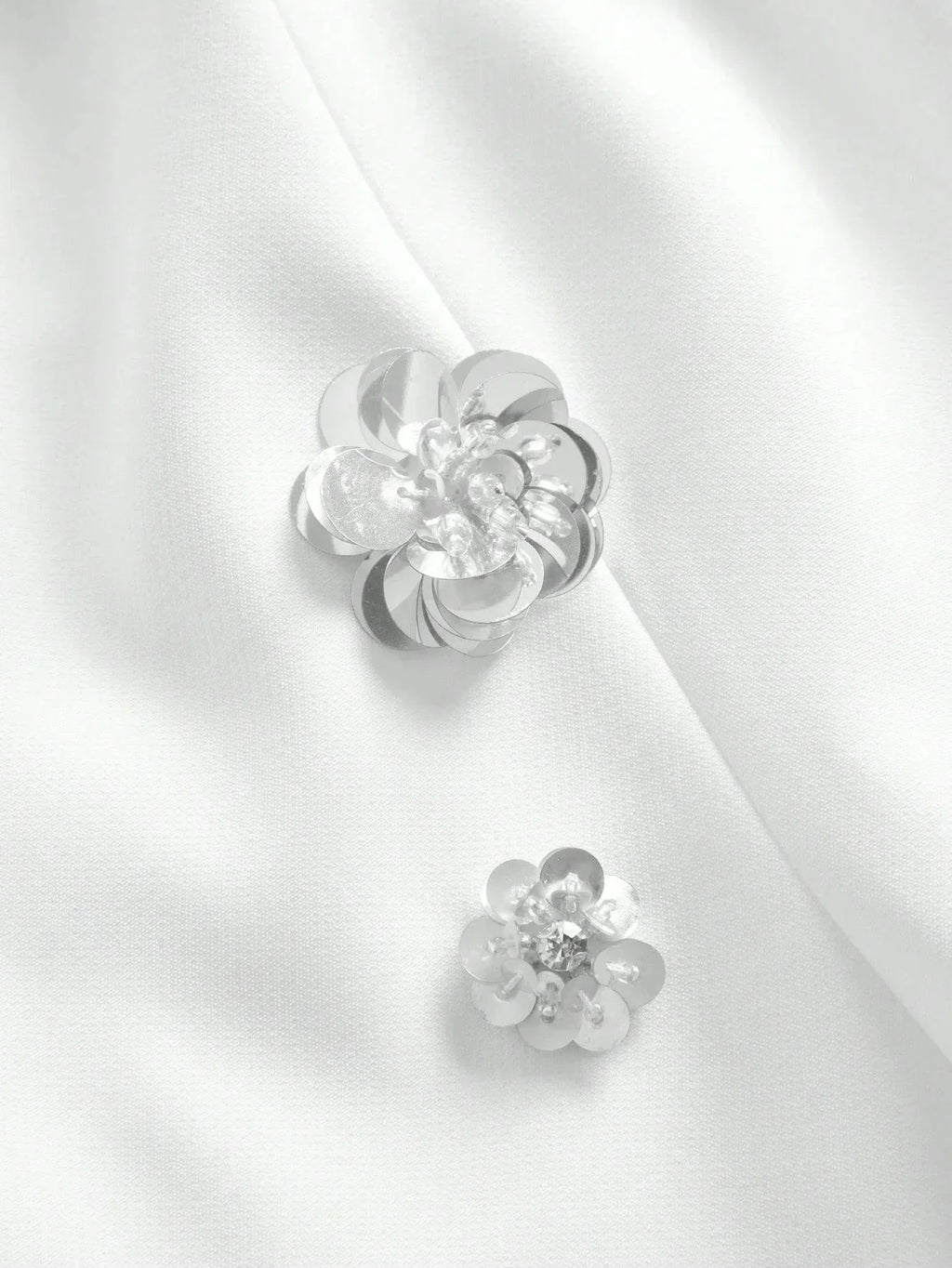 Delicate silver floral embellishments adorn a smooth white fabric, adding an elegant touch to this sophisticated dress. The.