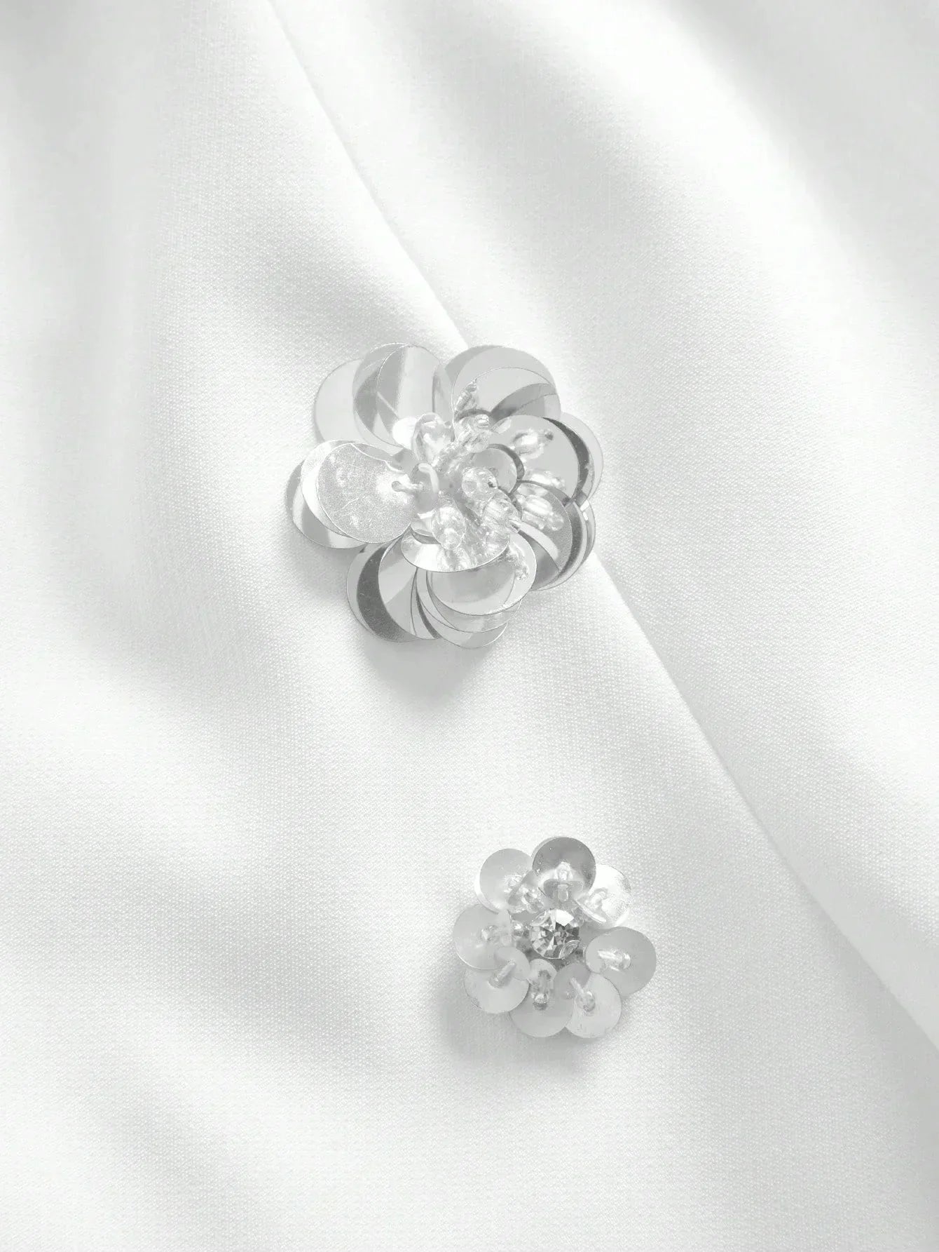 Delicate silver floral embellishments adorn a smooth white fabric, adding an elegant touch to this sophisticated dress. The.