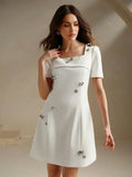 This elegant white dress features a chic square neckline and short sleeves, gracefully accentuated by shimmering floral.