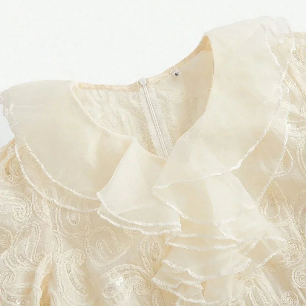 Delicate and ethereal, this cream-colored dress features a charming ruffled collar and intricate floral embroidery, giving.