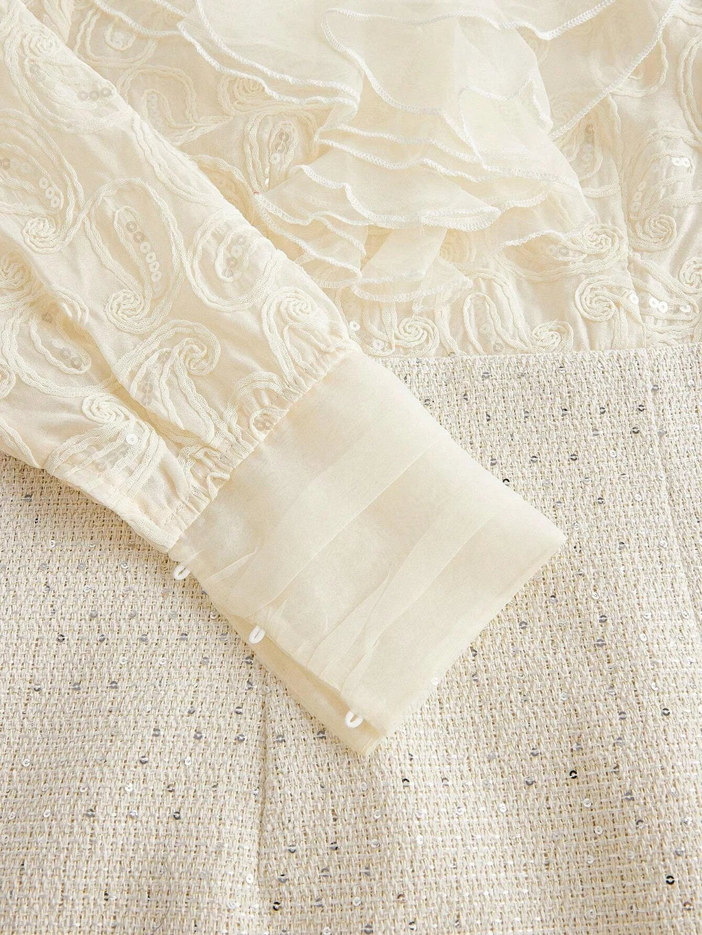 This elegant cream dress features intricate pastel embroidery and delicate flowing ruffles, creating a romantic and.