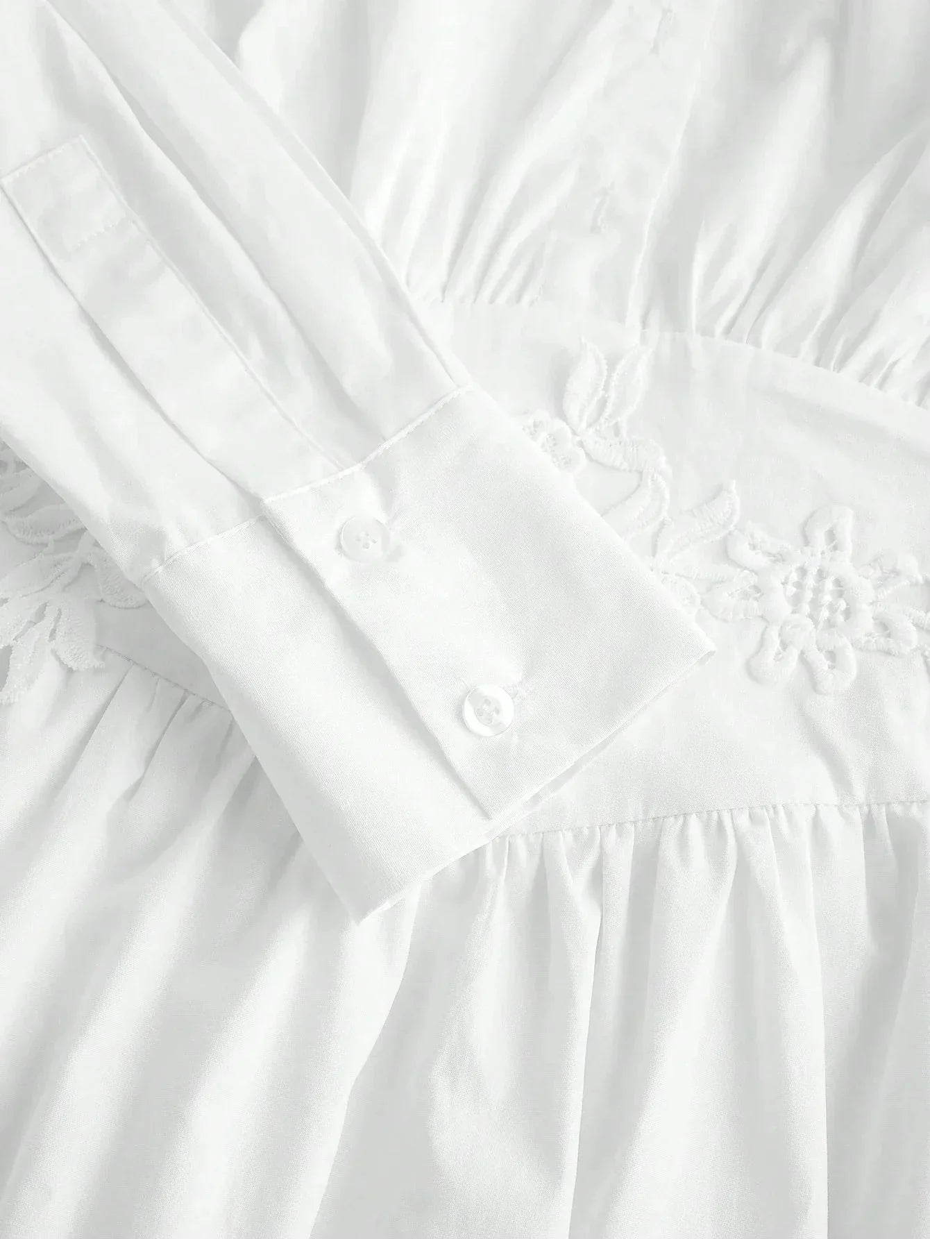 This elegant white dress features a delicate embroidered waistline, long sleeves with buttoned cuffs, and a soft, flowing.