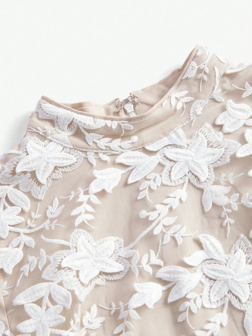 Elegant beige dress adorned with intricate white floral embroidery, featuring a refined high neckline and a soft, flowing.