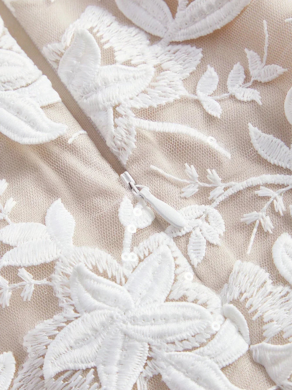 This elegant dress features a soft beige fabric adorned with intricate white floral embroidery, creating a delicate and.