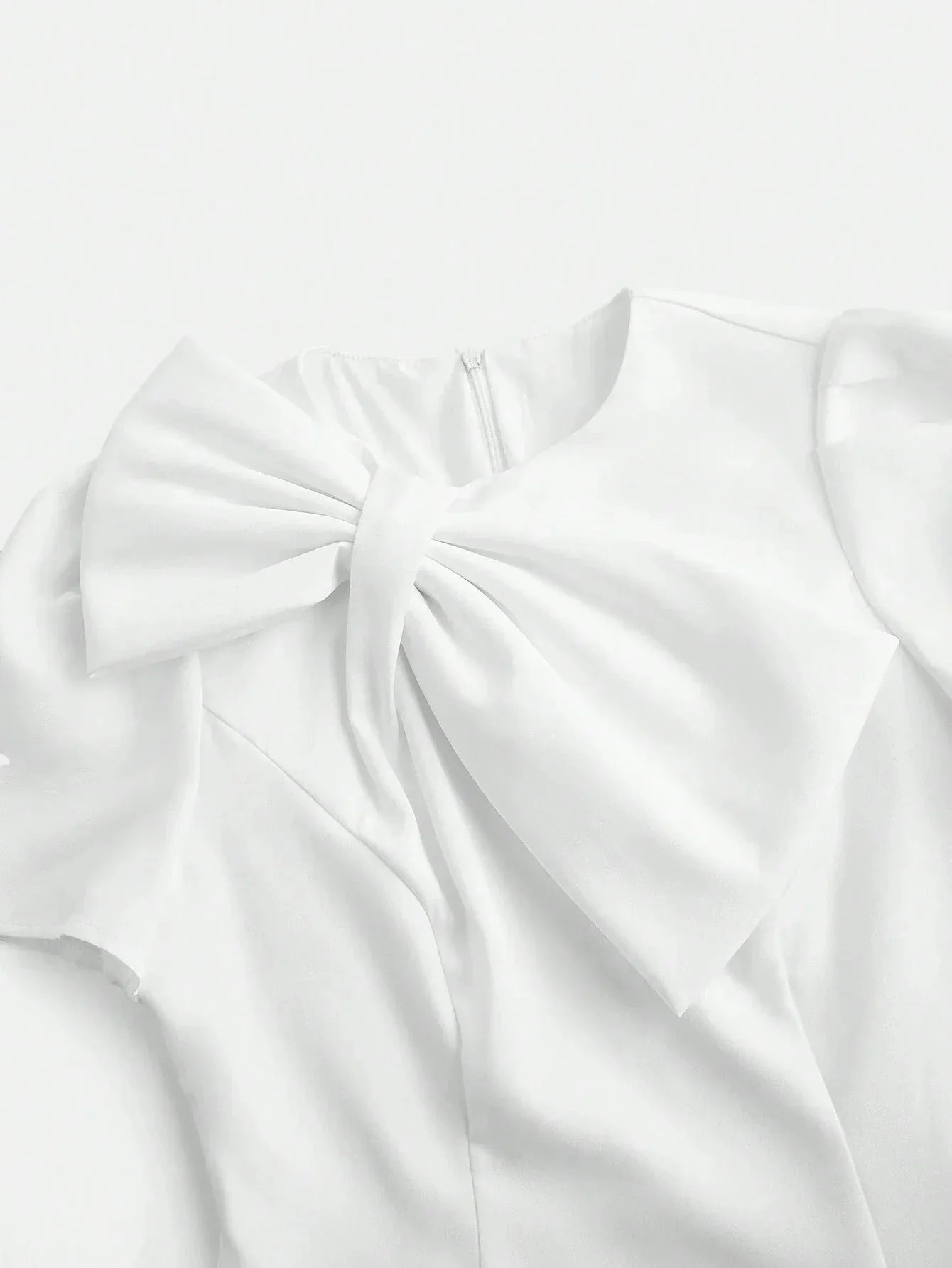 This elegant white dress features a sophisticated bow detail at the neckline, crafted from lightweight, flowing fabric that.
