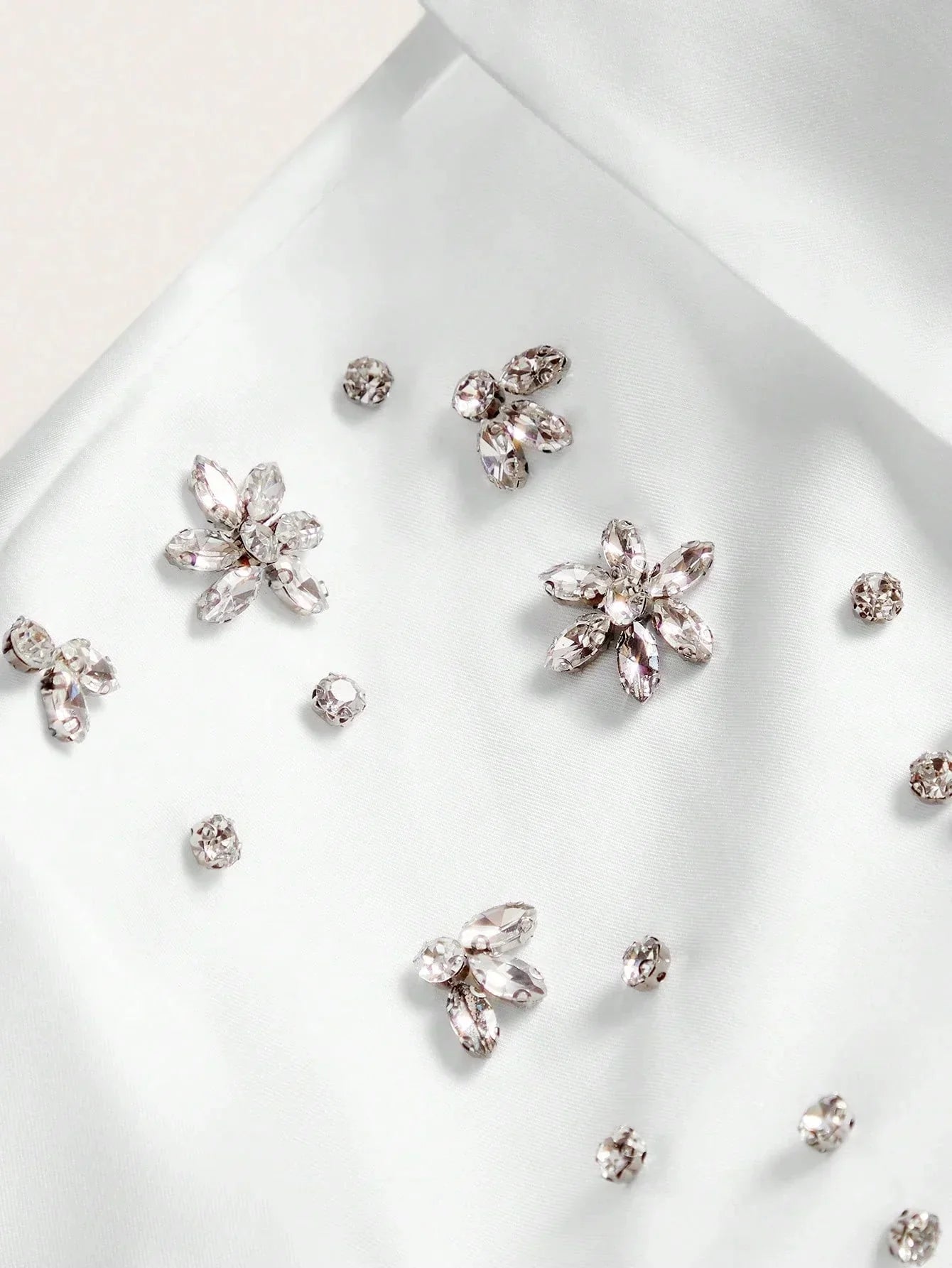 Delicate white satin fabric adorned with sparkling jewel embellishments in floral shapes creates a breathtakingly elegant.