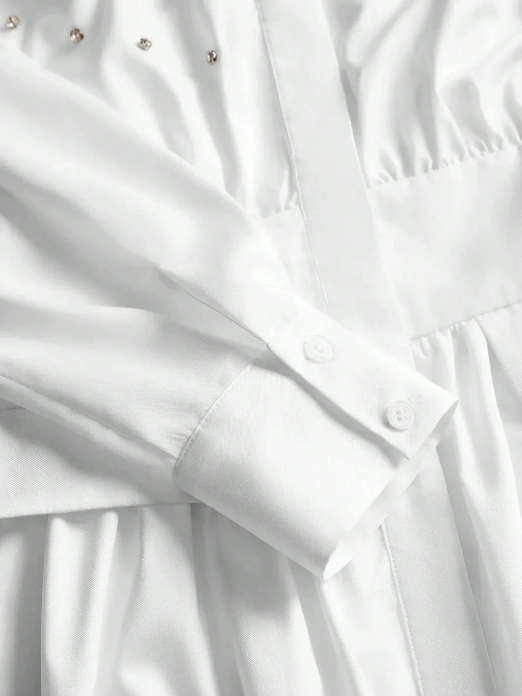 This elegant white dress features a sophisticated button-up design with delicate detailing along the bodice, complemented by.