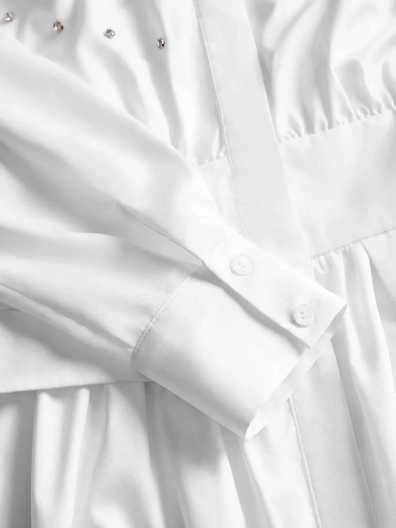 This elegant white dress features a sophisticated button-up design with delicate detailing along the bodice, complemented by.