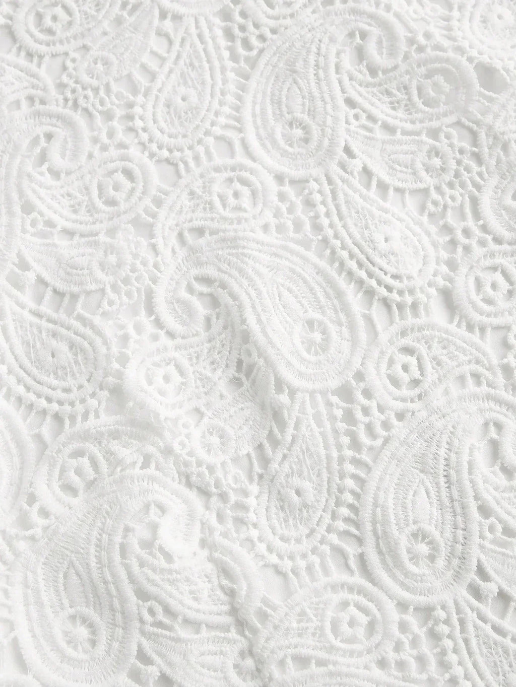 Delicate white lace fabric features an intricate paisley pattern, creating an elegant and airy look perfect for warm-weather.