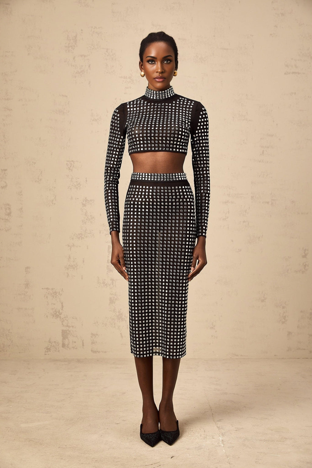 Woman wearing a black twopiece outfit consisting of a rhinestoneembellished mesh top and matching skirt