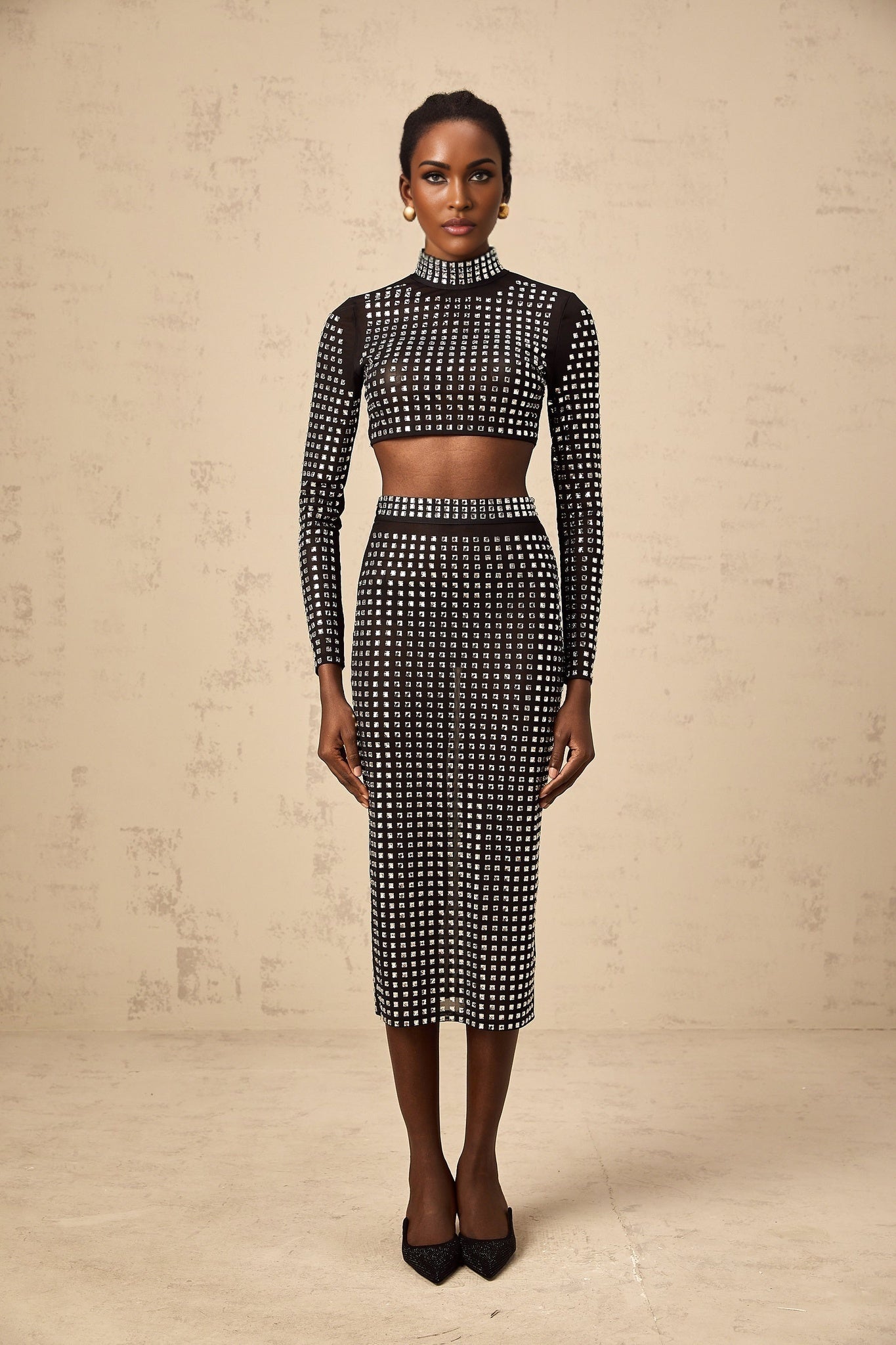 Woman wearing a black twopiece outfit consisting of a rhinestoneembellished mesh top and matching skirt